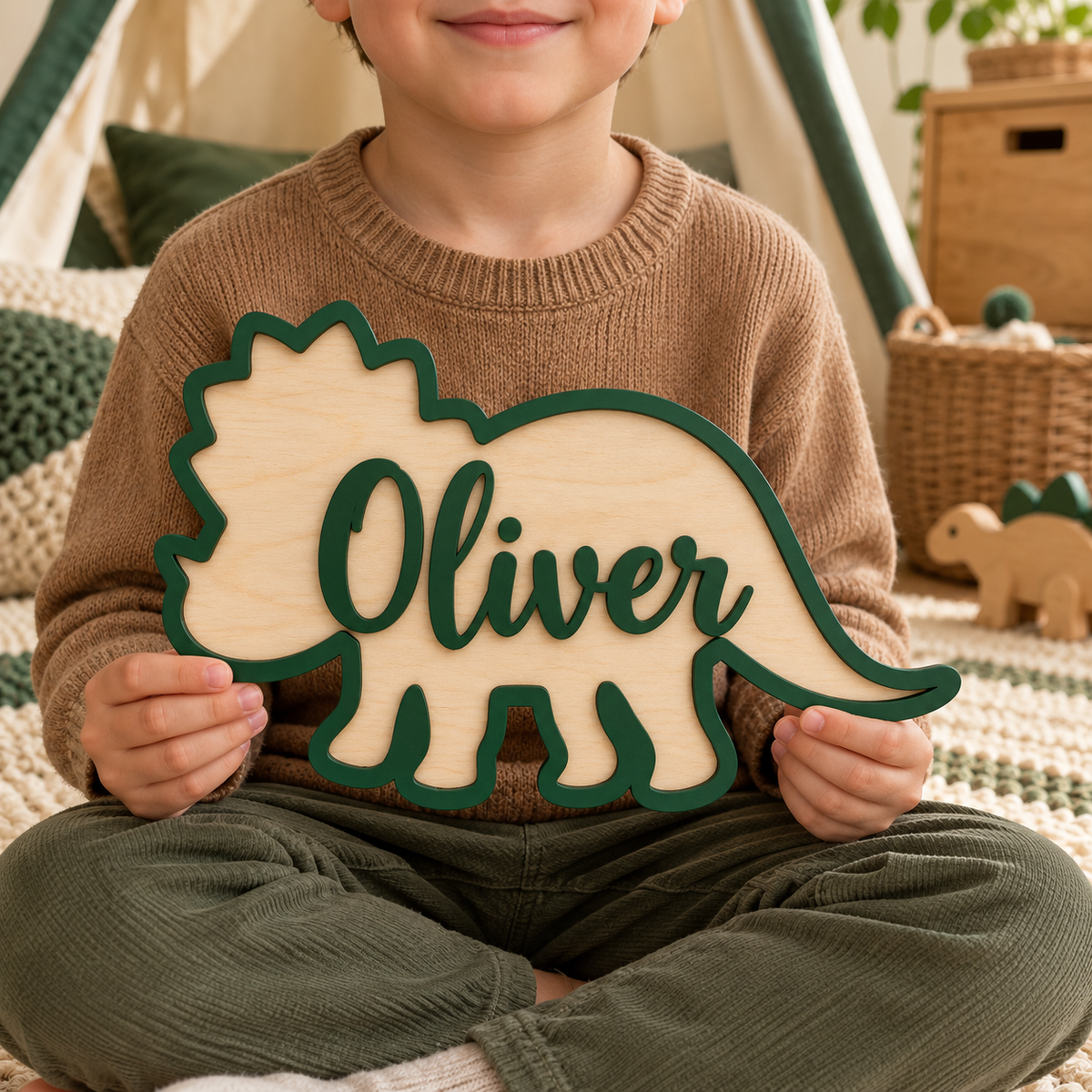 Child holding a forest green Oliver personalised wooden triceratops name sign in a cosy woodland play corner.