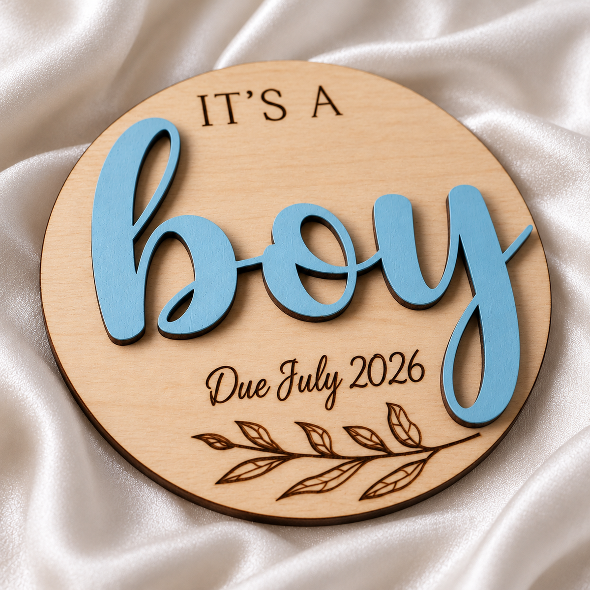 It's a Boy wooden gender reveal plaque close-up showing raised blue lettering and dark engraving, with Due July 2026 engraving