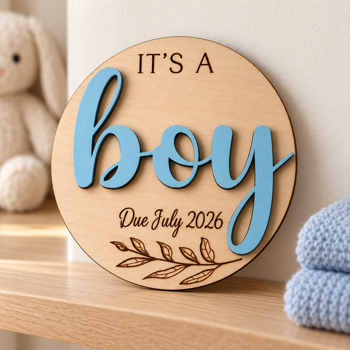 It's a Boy wooden gender reveal plaque displayed on a nursery shelf with Due July 2026 engraving