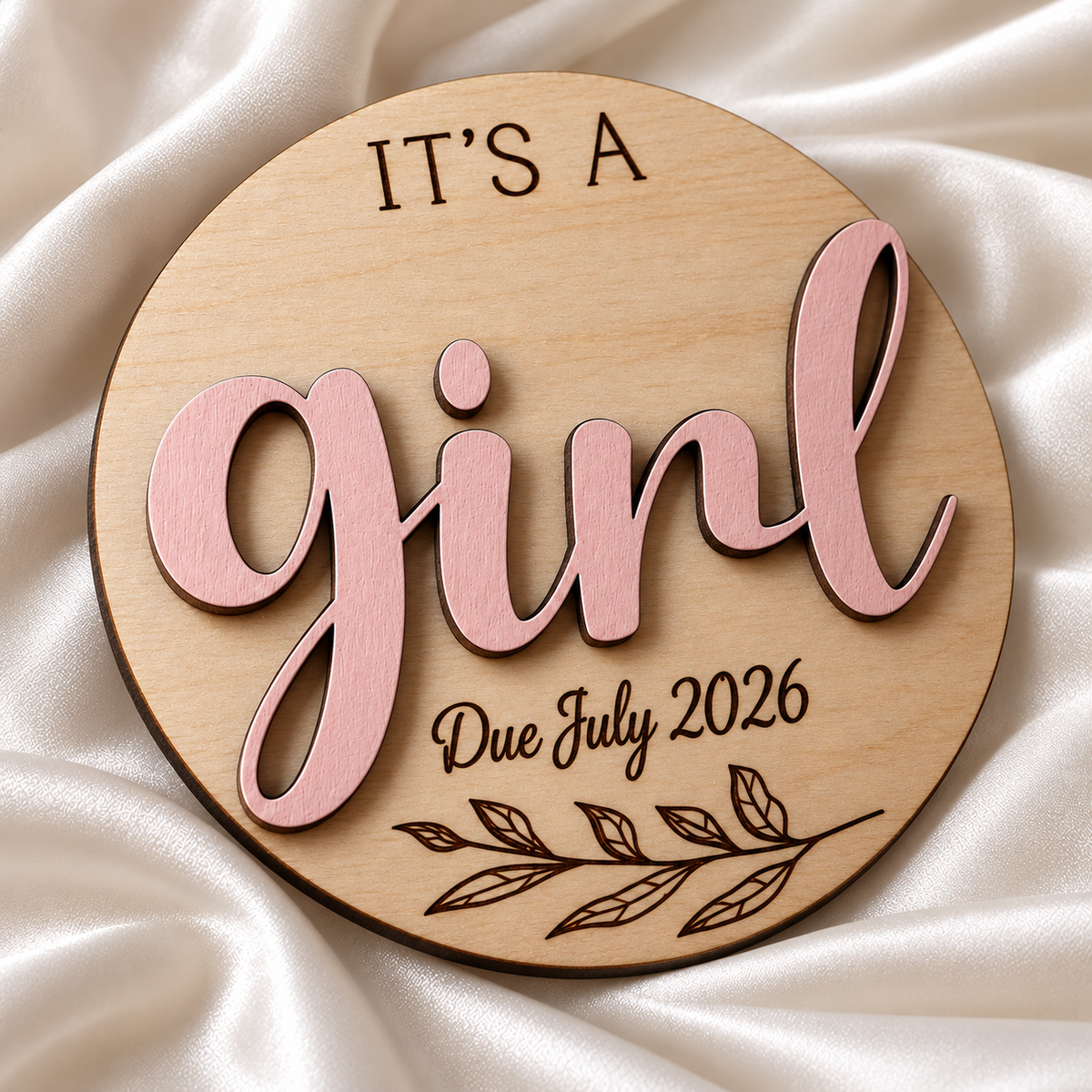 It's a Girl wooden gender reveal plaque close-up showing raised lettering and dark engraving, with Due July 2026 engraving