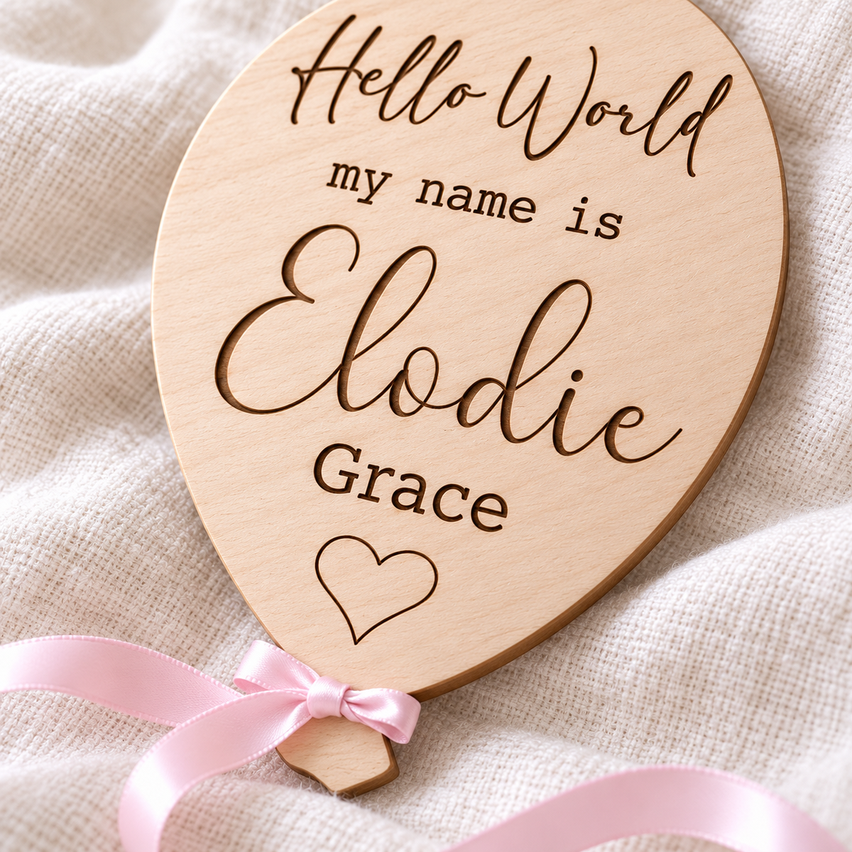 Close-up of dark laser engraving, natural birch grain and pink satin ribbon on the Elodie Grace baby announcement plaque.
