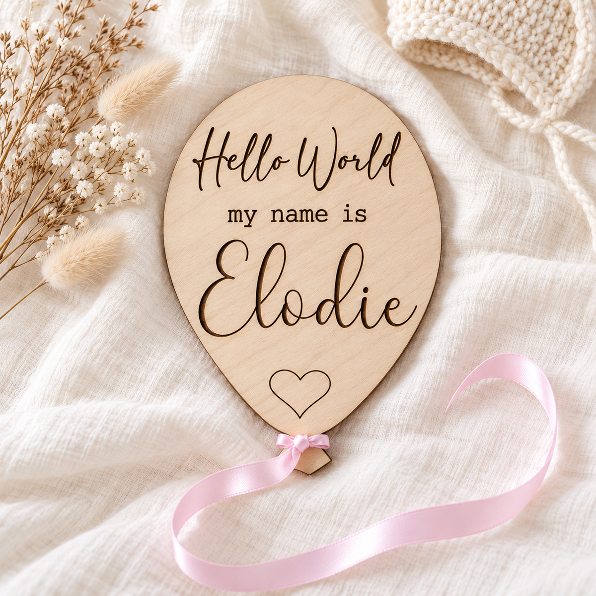 Single-name Elodie Hello World baby announcement plaque with an engraved heart and pink satin ribbon on ivory muslin.
