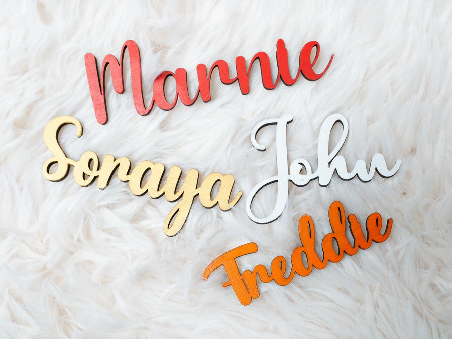 Colorful wooden name cutouts (Mannie, Soraya, John, Freddie) on white fur background.