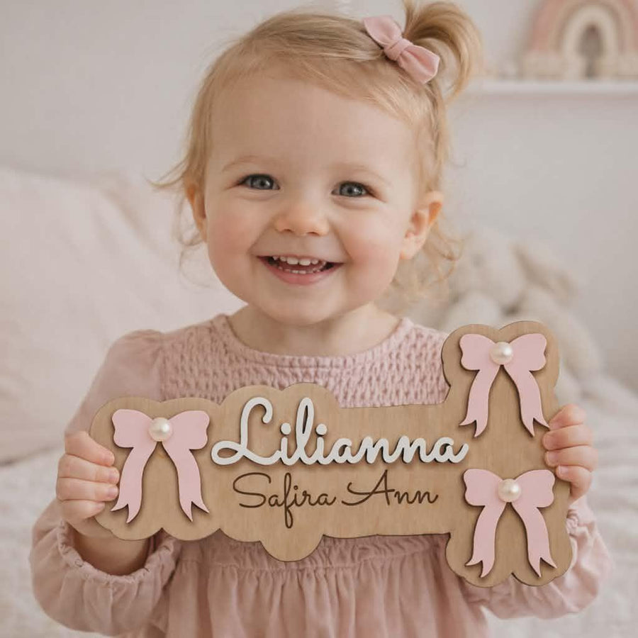 Smiling little girl holding a personalised bow name sign.