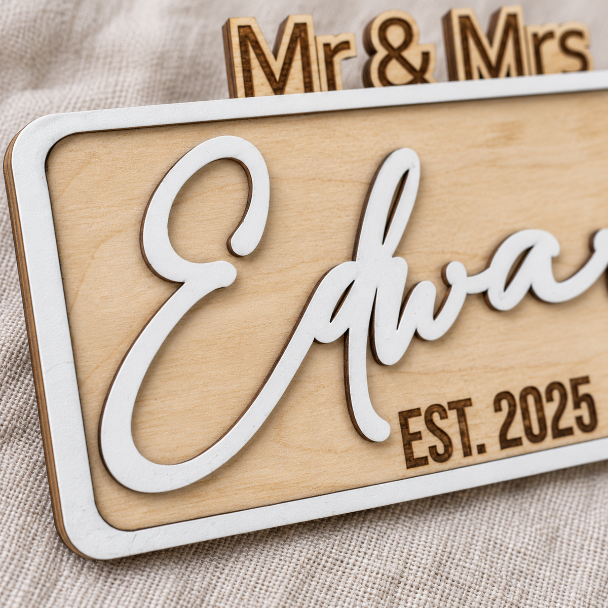 Close-up of the raised white surname lettering, painted frame and dark engraved year on the wooden wedding sign