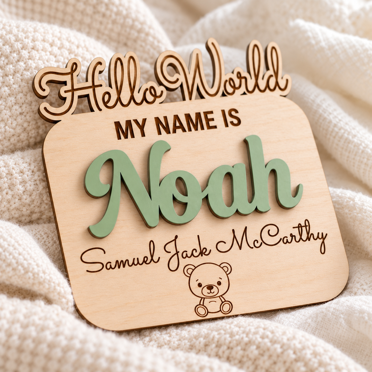 Close-up of Sage Green raised Noah lettering, crisp engraved extra names and teddy detail on the shaped birch newborn name sign.