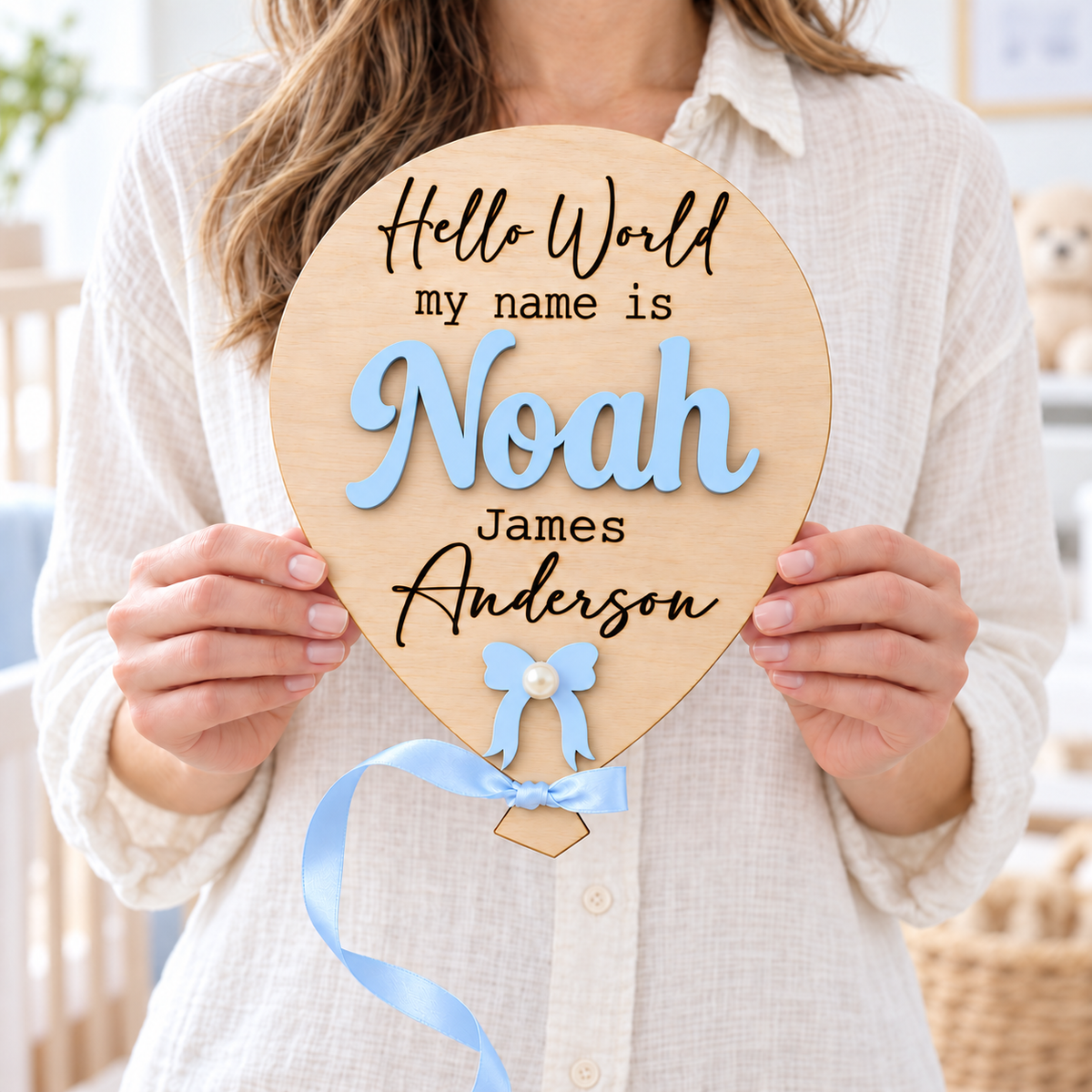 Pastel Blue Noah wooden balloon name sign held by a mother, with engraved James Anderson and blue ribbon.