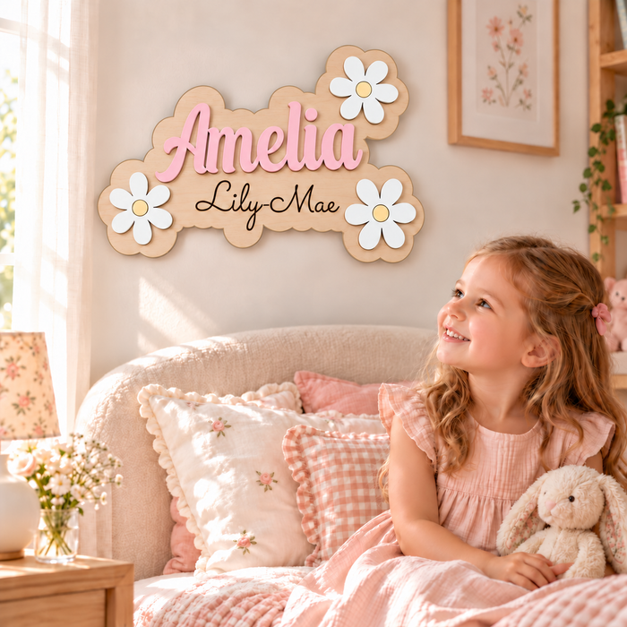 Personalised Amelia wooden name sign with black Lily-Mae engraving, pastel pink lettering and white daisies, displayed in a girl's bedroom.
