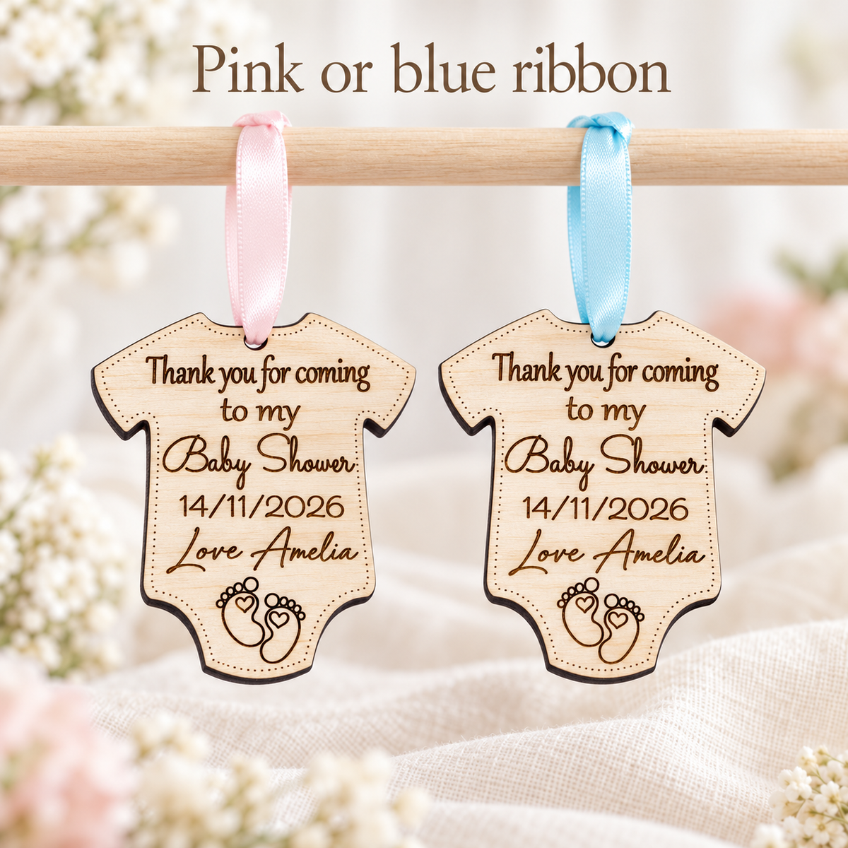 Personalised wooden bodysuit baby shower favours hanging from pink and blue satin ribbons.