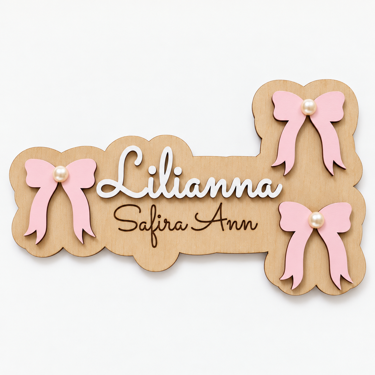 Close-up of the layered wooden bow name sign, white raised Lilianna lettering, dark Safira Ann engraving and pearl details.