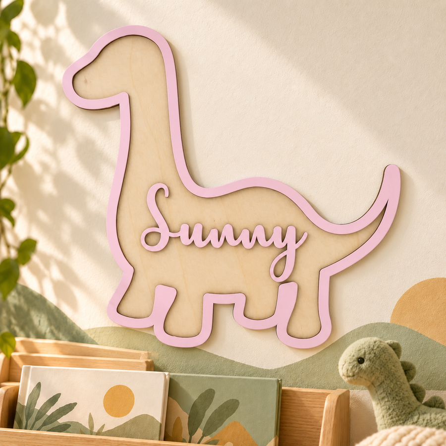 Personalised wooden brachiosaurus name sign in pastel pink, displayed on a nursery wall with the name Sunny