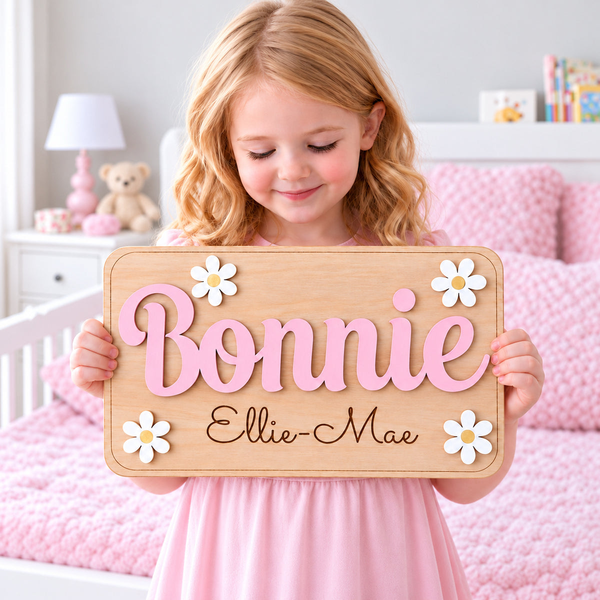 Square hero photo of a girl holding a Bonnie wooden daisy door sign with pastel pink raised name and Ellie-Mae engraved below