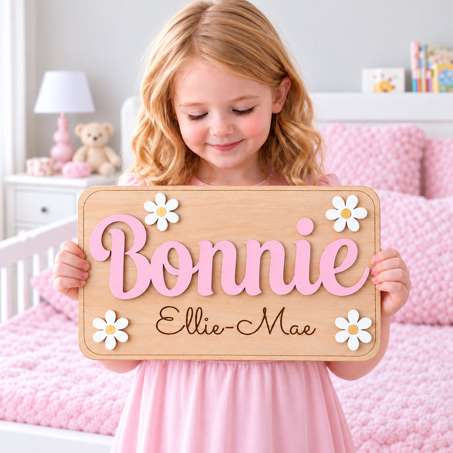 Square hero photo of a girl holding a Bonnie wooden daisy door sign with pastel pink raised name and Ellie-Mae engraved below