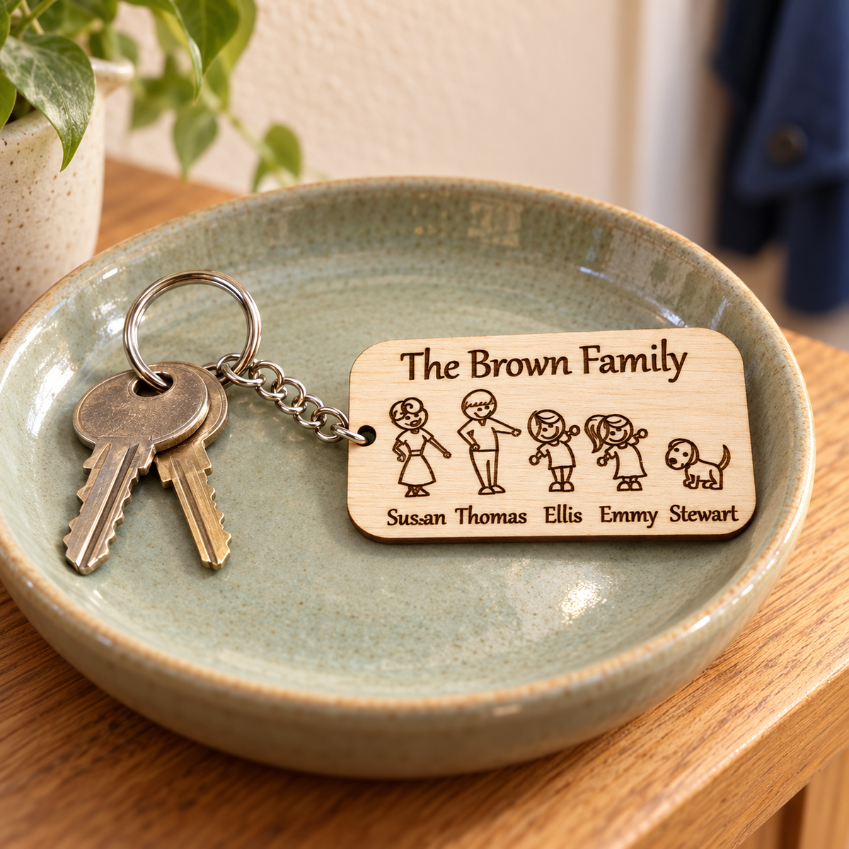 Engraved wooden family keyring with names and a dog, attached to two house keys in a sage ceramic dish