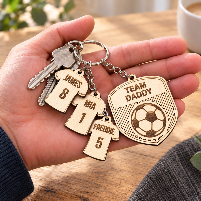 Personalised wooden football keyring in a hand, with Team Daddy badge and James 8, Mia 1 and Freddie 5 shirt charms