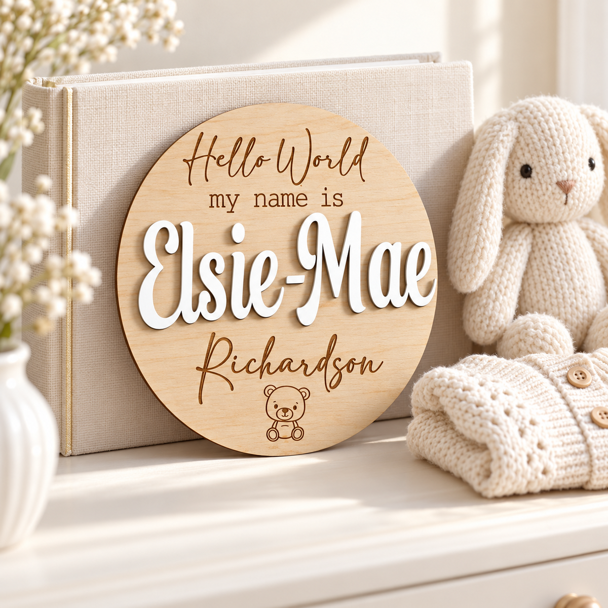 Round teddy bear name plaque with raised White Elsie-Mae lettering and engraved Richardson surname styled with baby keepsakes.