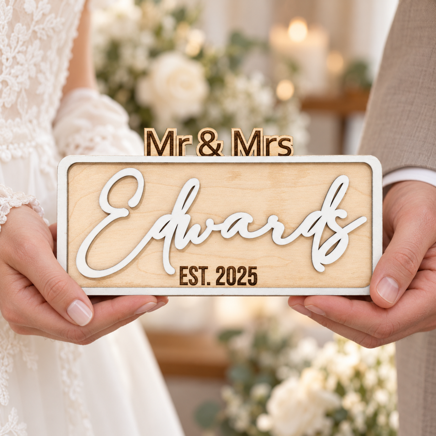 Bride and groom holding a white personalised Mr & Mrs wooden wedding sign with Edwards surname and EST. 2025