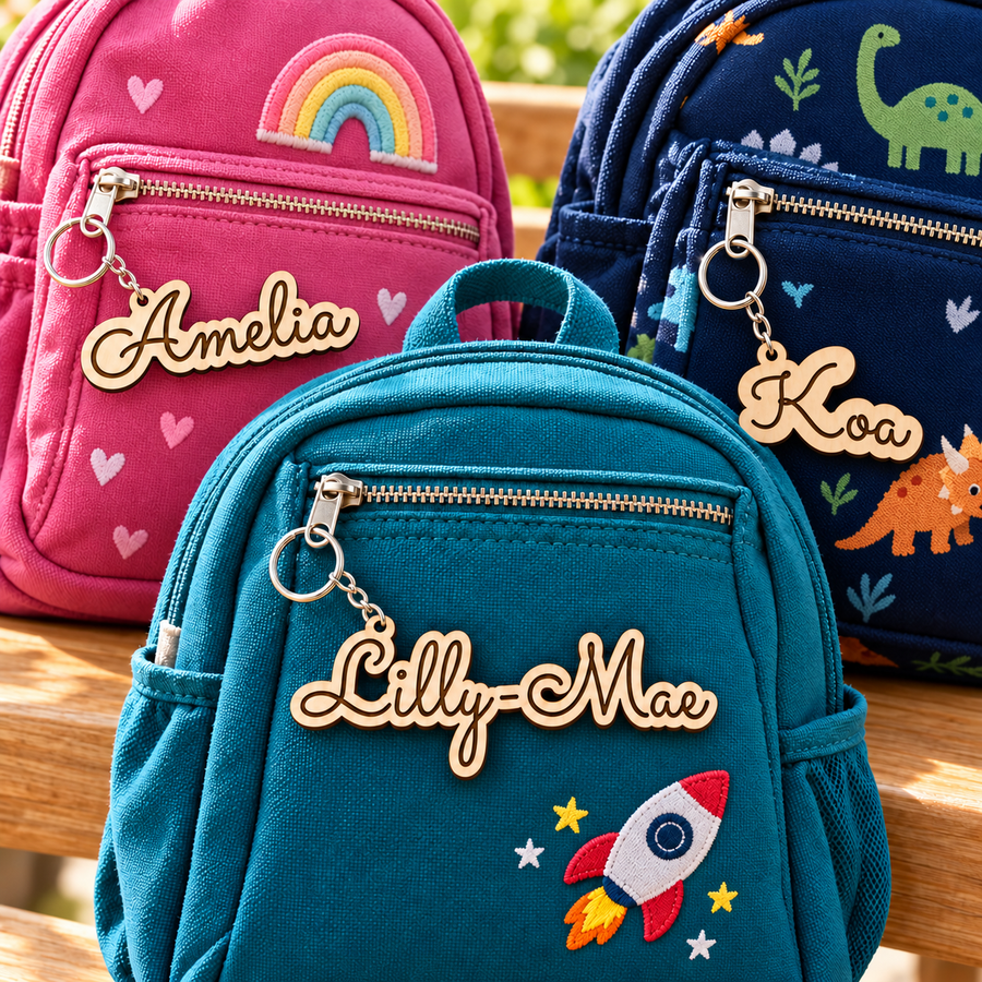 Personalised wooden name keyrings for Lilly-Mae, Amelia and Koa attached to three children's backpacks.