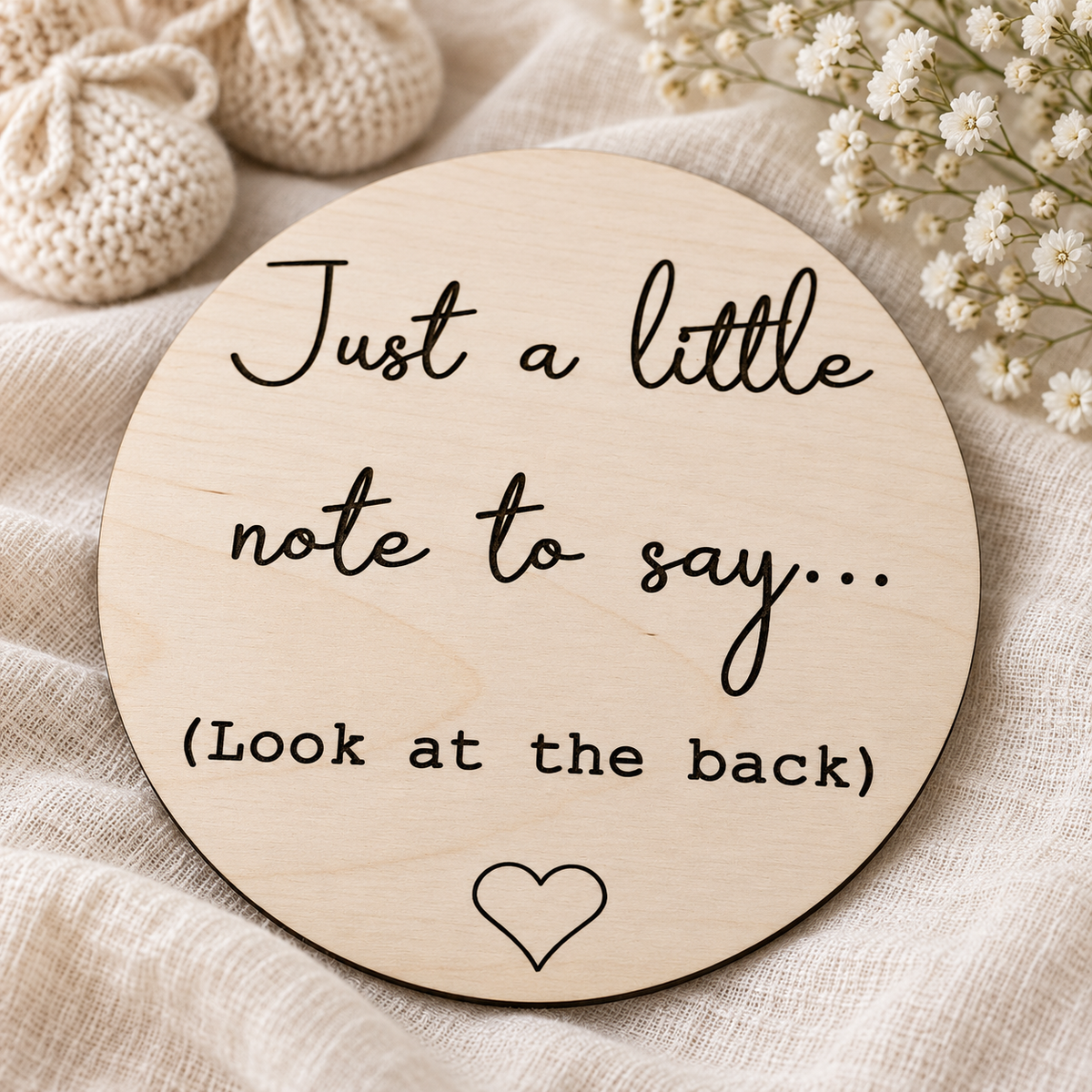Front of the double-sided pregnancy reveal plaque styled with cream baby booties and white flowers