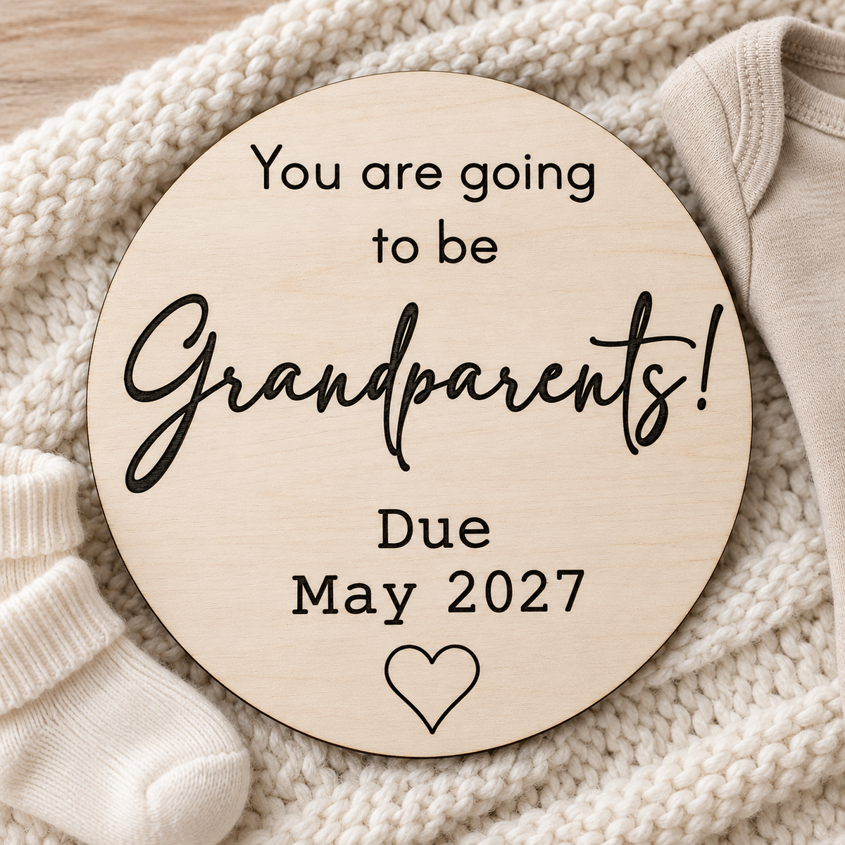Wooden grandparents pregnancy announcement plaque with personalised due date styled beside baby socks and neutral clothing