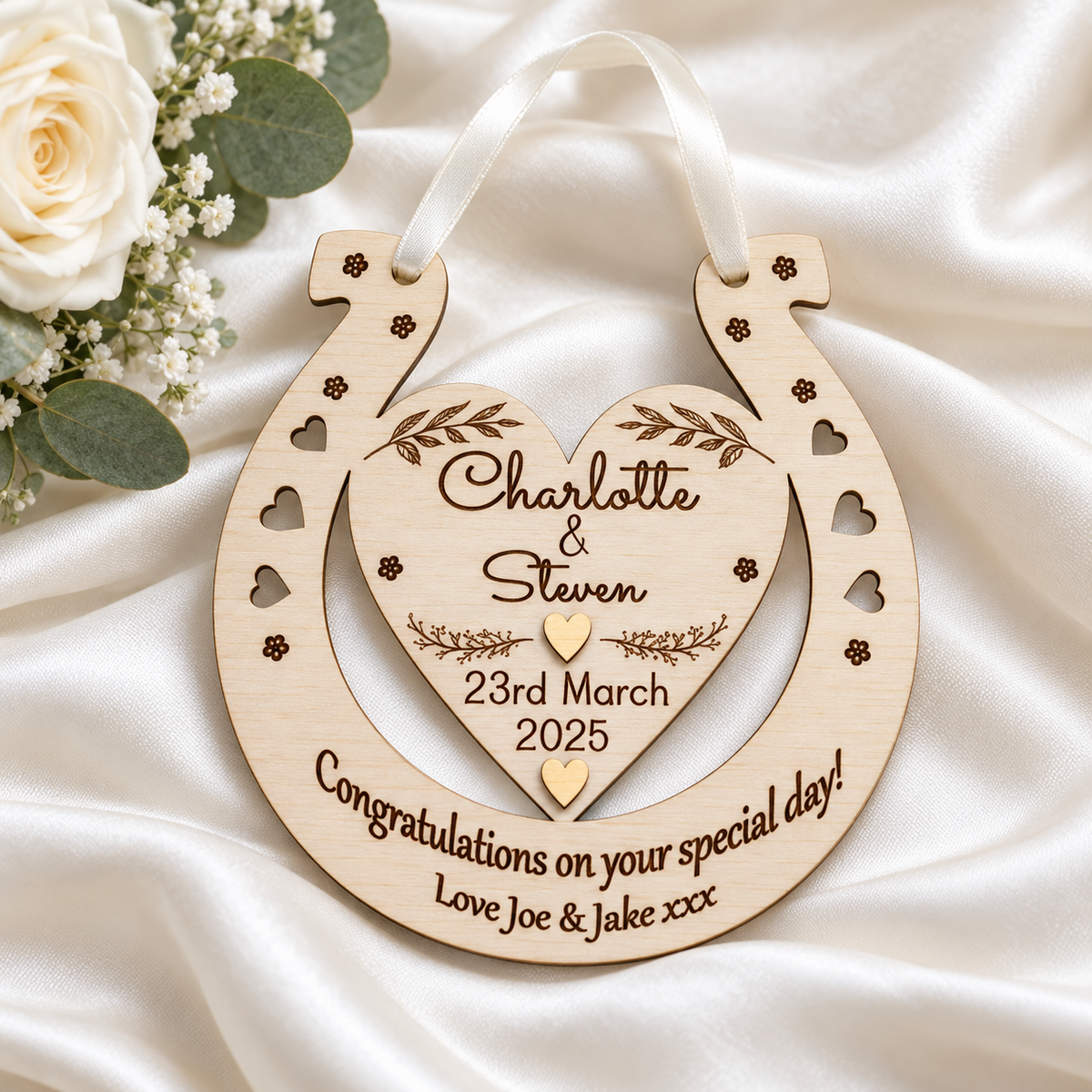 Wooden wedding horseshoe with Charlotte and Steven's names and a wedding message on ivory satin beside white roses