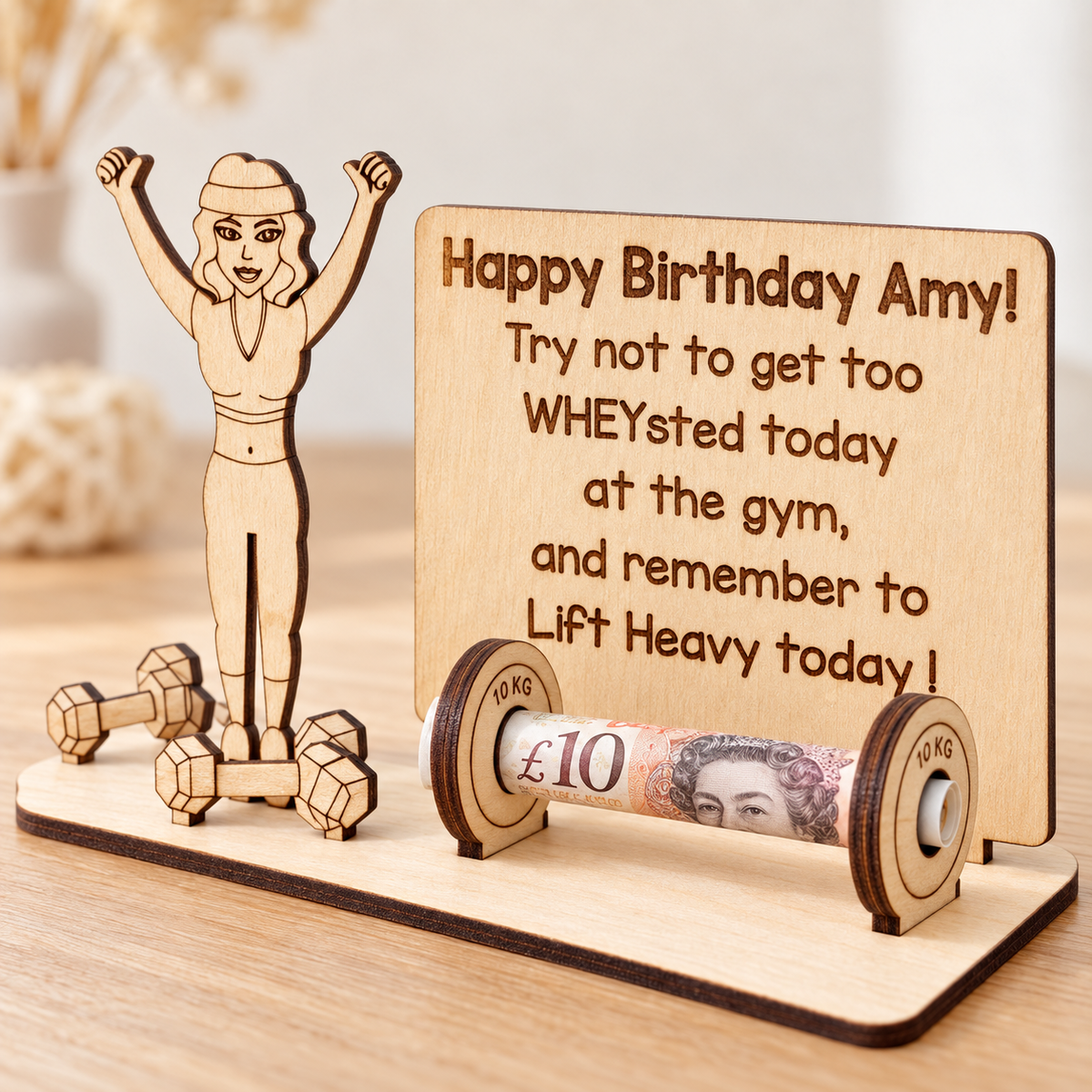Close-up of the laser-engraved birthday message and wooden weight plates holding a rolled banknote
