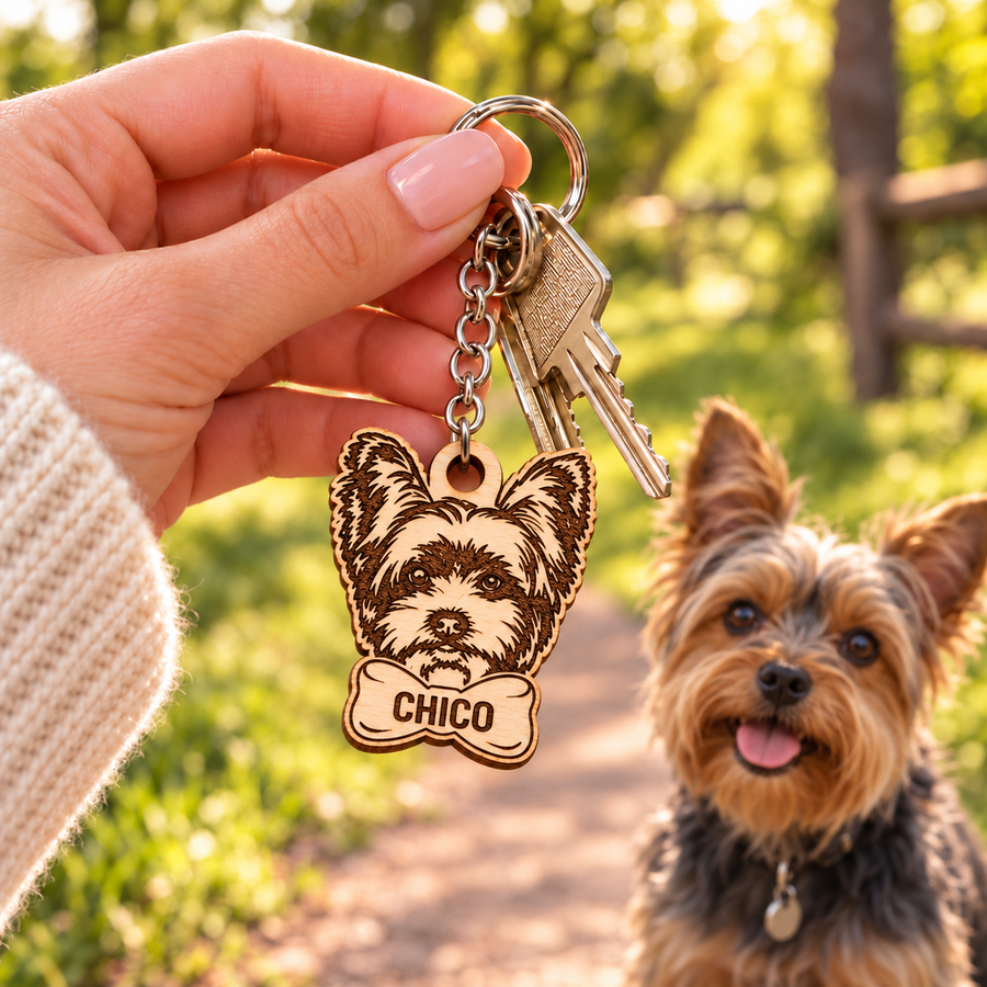 Personalised wooden Yorkie keyring engraved CHICO, held with keys on a woodland walk with a Yorkshire Terrier in the background